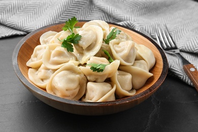 Photo of Tasty dumplings with parsley in bowl on black table