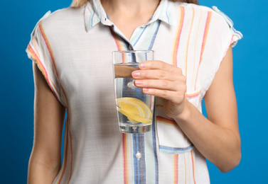 Photo of Young woman with glass of lemon water on light blue background, closeup