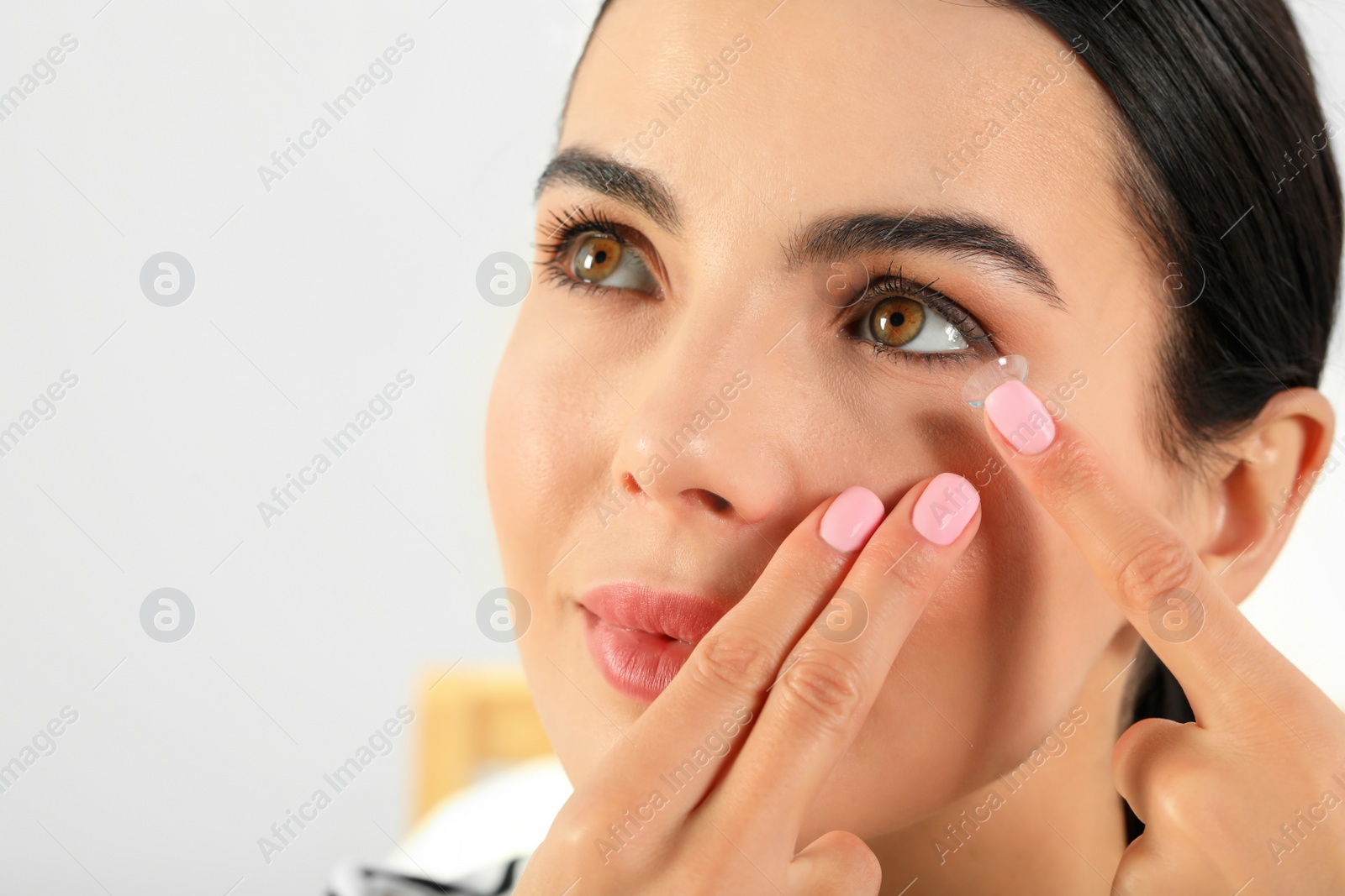 Photo of Young woman putting contact lens in her eye, closeup