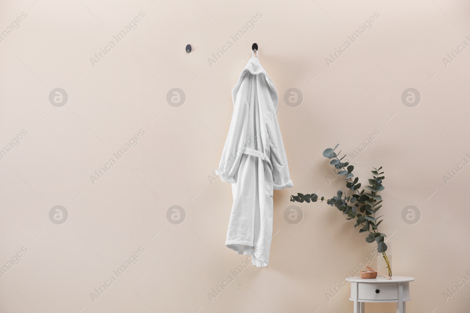 Photo of Soft comfortable bathrobe hanging on beige wall indoors, space for text