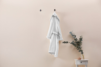 Photo of Soft comfortable bathrobe hanging on beige wall indoors, space for text