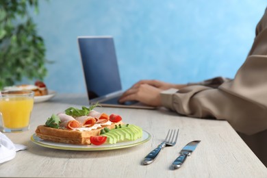 Photo of Woman working with laptop at wooden table during breakfast