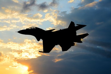 Silhouette of jet fighter in cloudy sky at sunrise