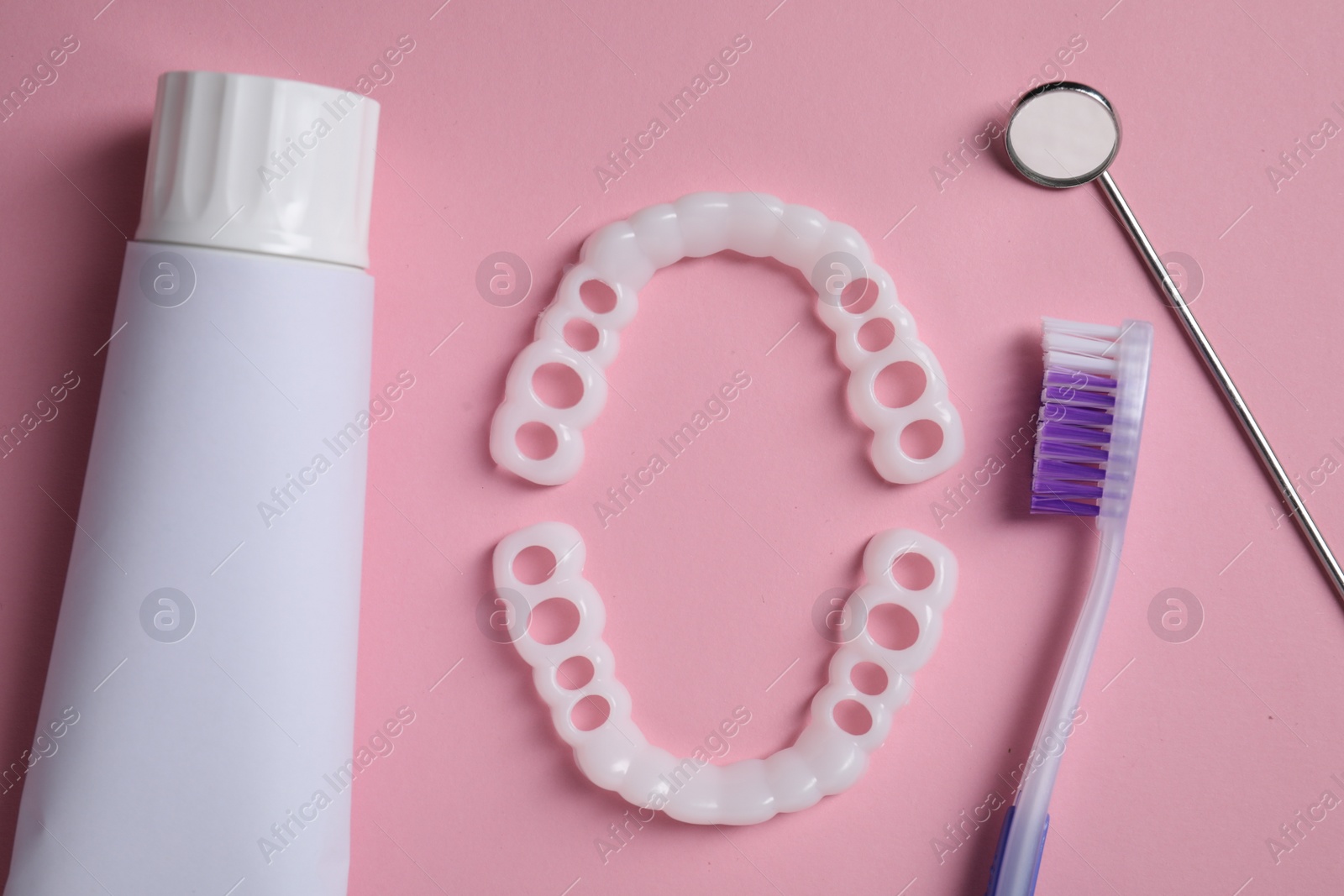 Photo of Bite correction. Toothpaste, brush, dentist mirror and dental mouth guards on pink background, flat lay