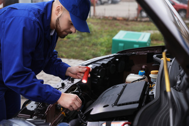 Photo of Young mechanic with flashlight fixing car outdoors