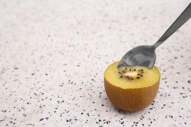 Photo of Spoon in fresh ripe yellow kiwi on white table with pattern. Space for text