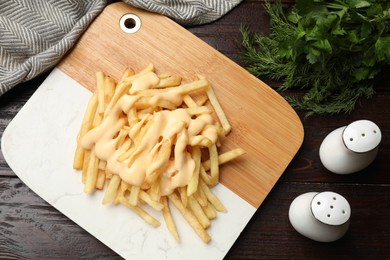 Photo of Delicious french fries with cheese sauce, greens and spice shakers on wooden table, flat lay