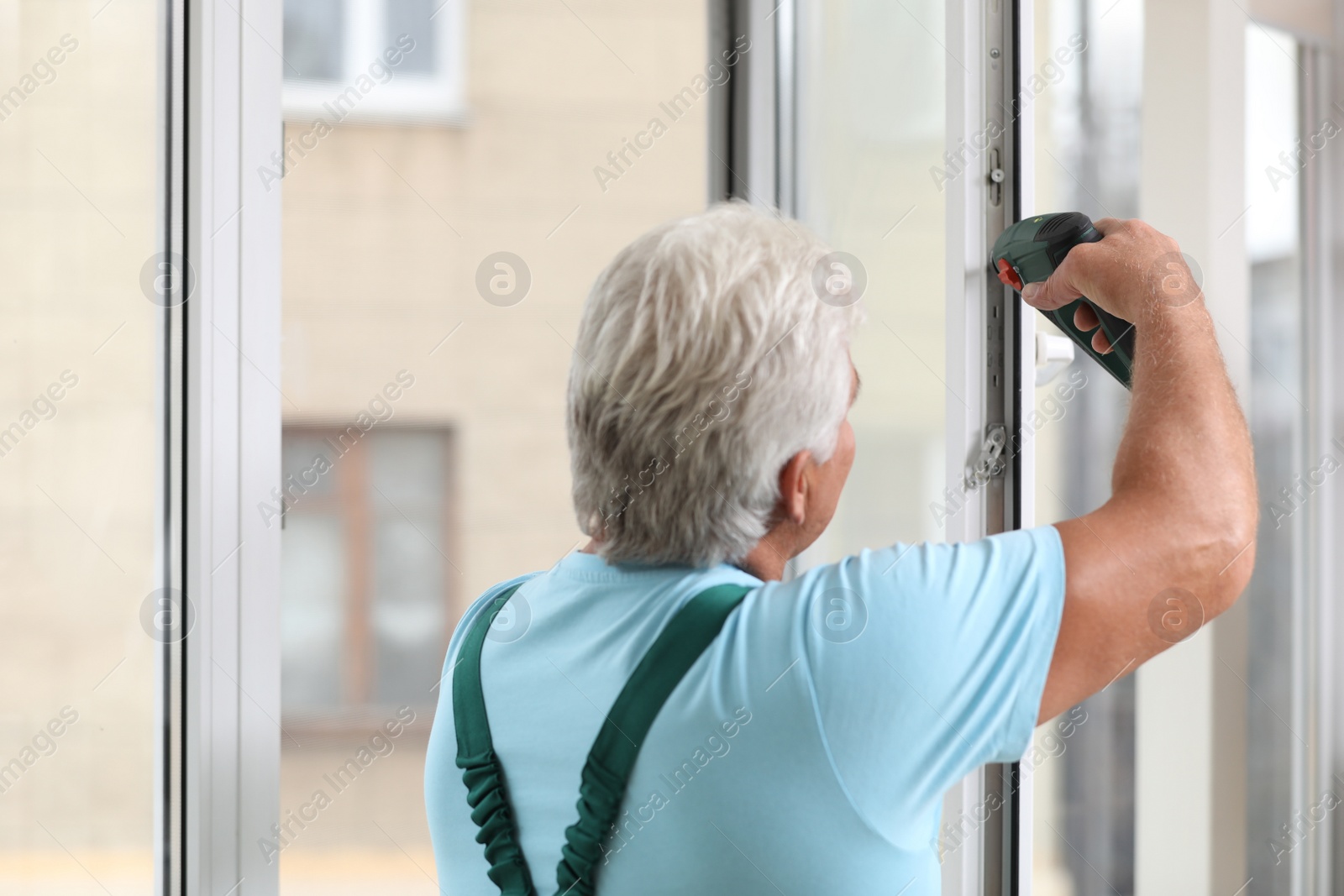 Photo of Mature construction worker repairing plastic window with electric screwdriver indoors