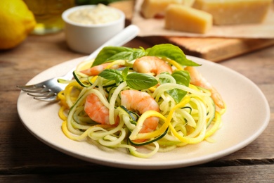 Photo of Delicious zucchini pasta with shrimps and basil on wooden table, closeup