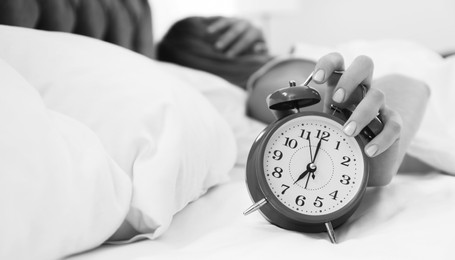 Image of Woman turning off alarm clock in bedroom, selective focus. Black and white photography