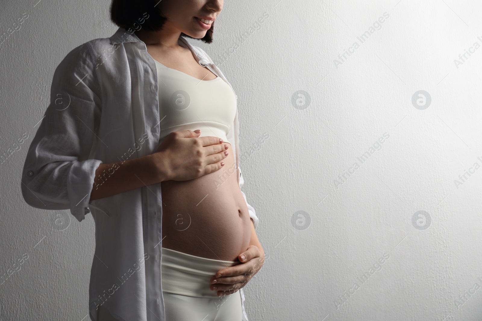 Photo of Pregnant young woman touching belly on light background, closeup. Space for text