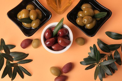 Photo of Bottle of oil, olives and tree twigs on orange background, flat lay