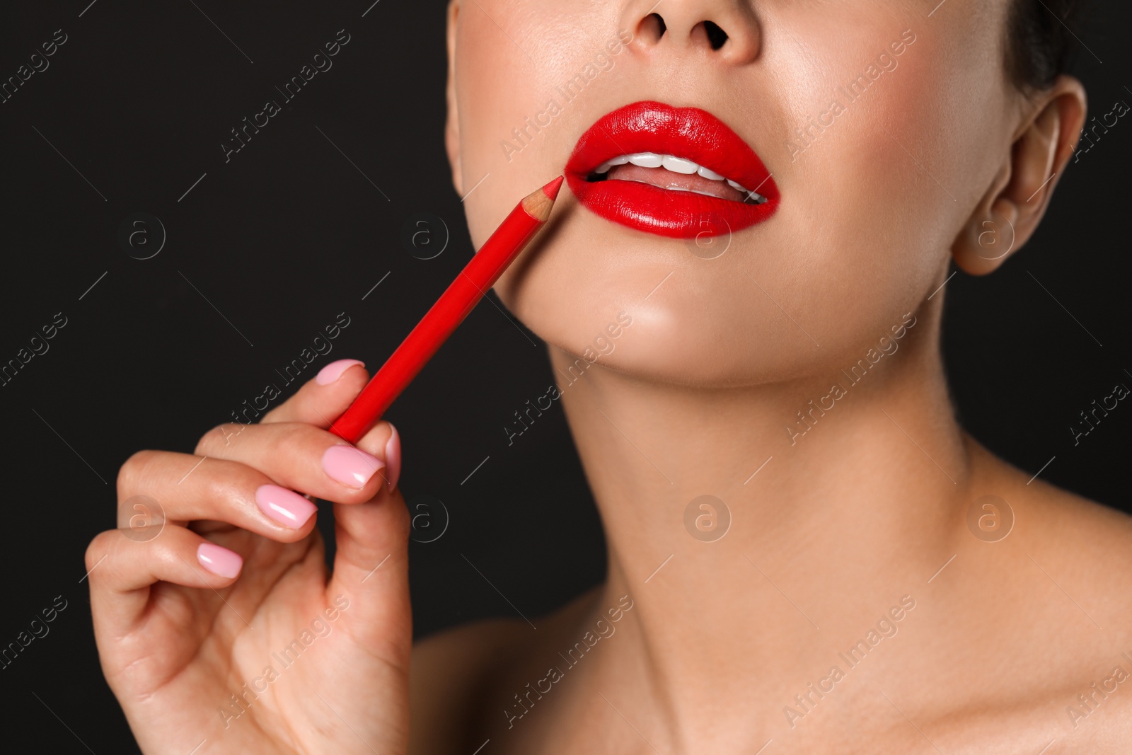 Photo of Young woman with beautiful red lip pencil on black background, closeup