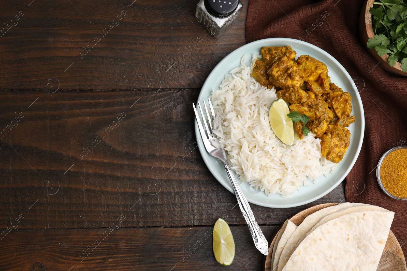 Photo of Delicious chicken curry with rice and ingredients on wooden table, flat lay. Space for text