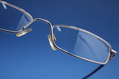 Photo of Stylish pair of glasses with metal frame on blue background, closeup