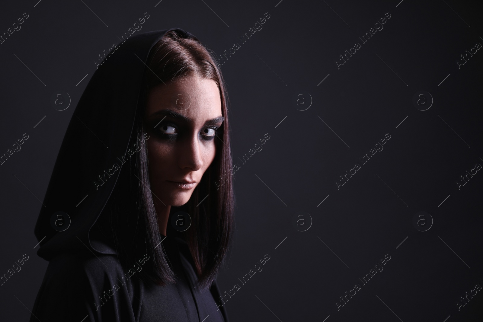 Photo of Mysterious witch with spooky eyes on black background, space for text