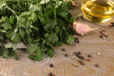 Bunch of raw parsley, oil, garlic and peppercorns on wooden table, closeup
