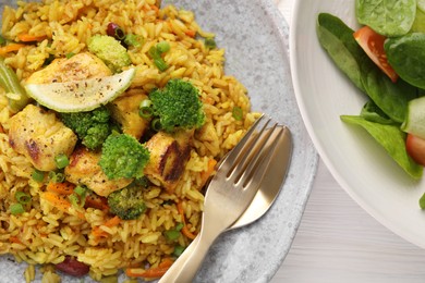 Photo of Tasty rice with meat and vegetables in plate served on white wooden table, flat lay