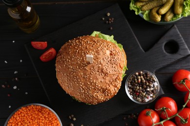 Photo of Tasty vegetarian burger and ingredients on black wooden table, flat lay