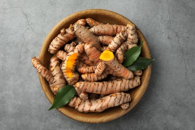 Photo of Bowl with raw turmeric roots and green leaves on grey table, top view