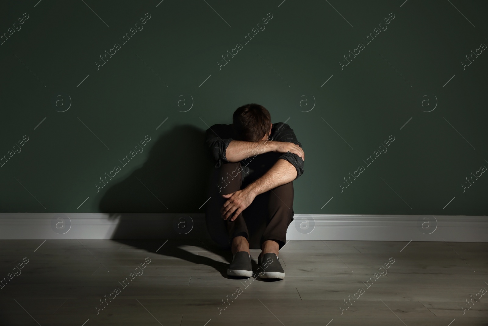 Photo of Depressed young man sitting on floor in darkness