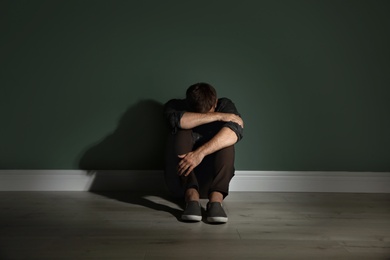 Photo of Depressed young man sitting on floor in darkness