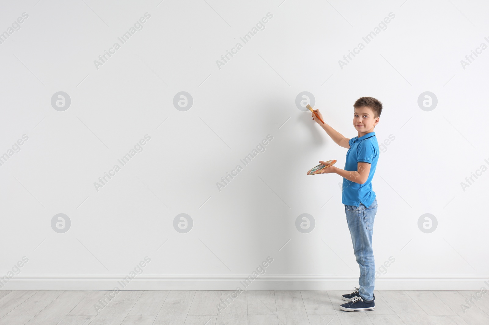 Photo of Little child painting on white wall indoors. Space for text