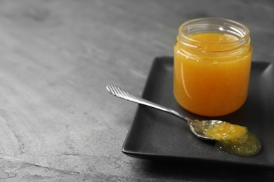 Photo of Delicious orange marmalade in jar and spoon on grey table. Space for text