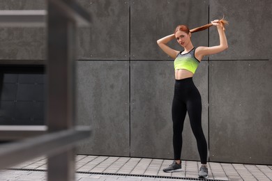 Beautiful woman in stylish gym clothes posing near grey wall on street