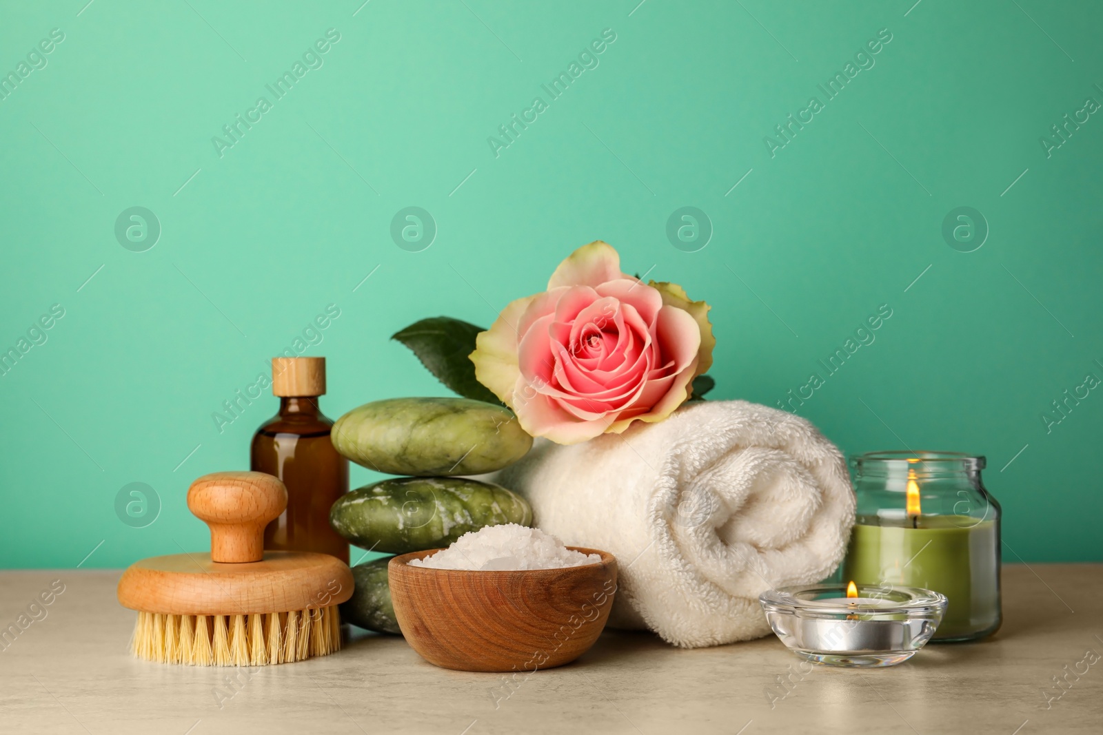 Photo of Composition with different spa products, candles and rose on beige table against turquoise background