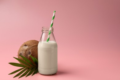 Glass bottle of delicious vegan milk, coconut and leaf on pink background, space for text