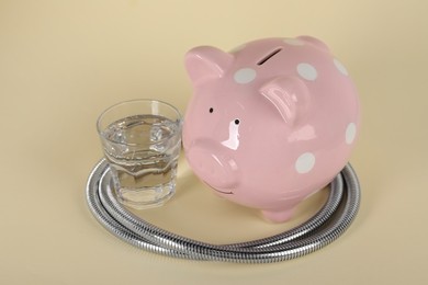 Photo of Water scarcity concept. Piggy bank, shower hose and glass of drink on beige background