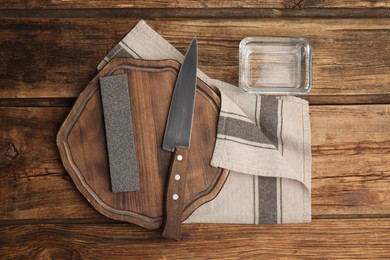 Photo of Sharpening stone, knife and water on wooden table, flat lay