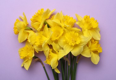 Photo of Beautiful daffodil bouquet on violet background, top view