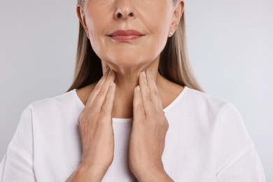 Photo of Endocrine system. Senior woman doing thyroid self examination on light grey background, closeup