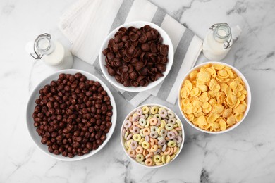 Photo of Different delicious breakfast cereals and milk on white marble table, flat lay