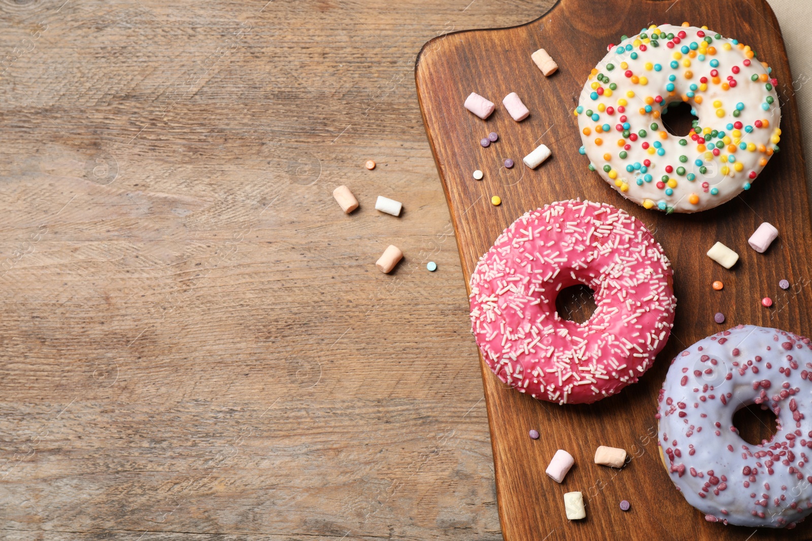 Photo of Top view of yummy donuts with sprinkles on wooden table, space for text