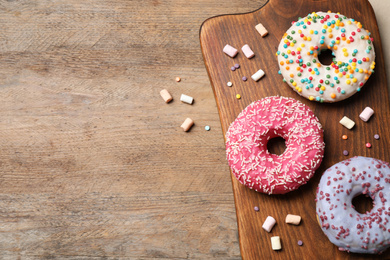Top view of yummy donuts with sprinkles on wooden table, space for text