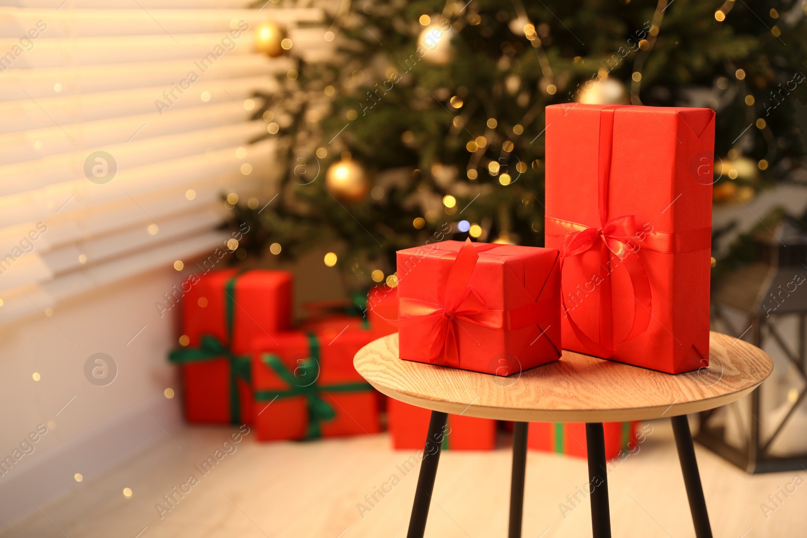 Photo of Beautifully wrapped Christmas gifts on wooden table in living room, space for text