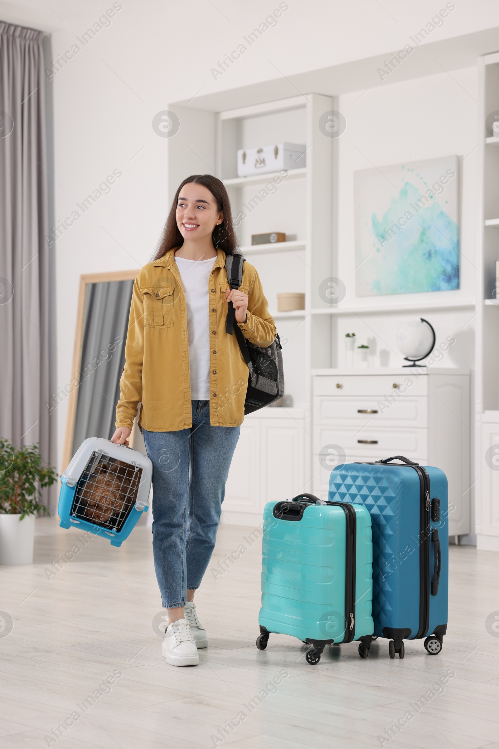 Photo of Travel with pet. Smiling woman with backpack holding carrier with dog at home