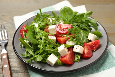 Delicious salad with feta cheese, arugula and tomatoes on wooden table, closeup