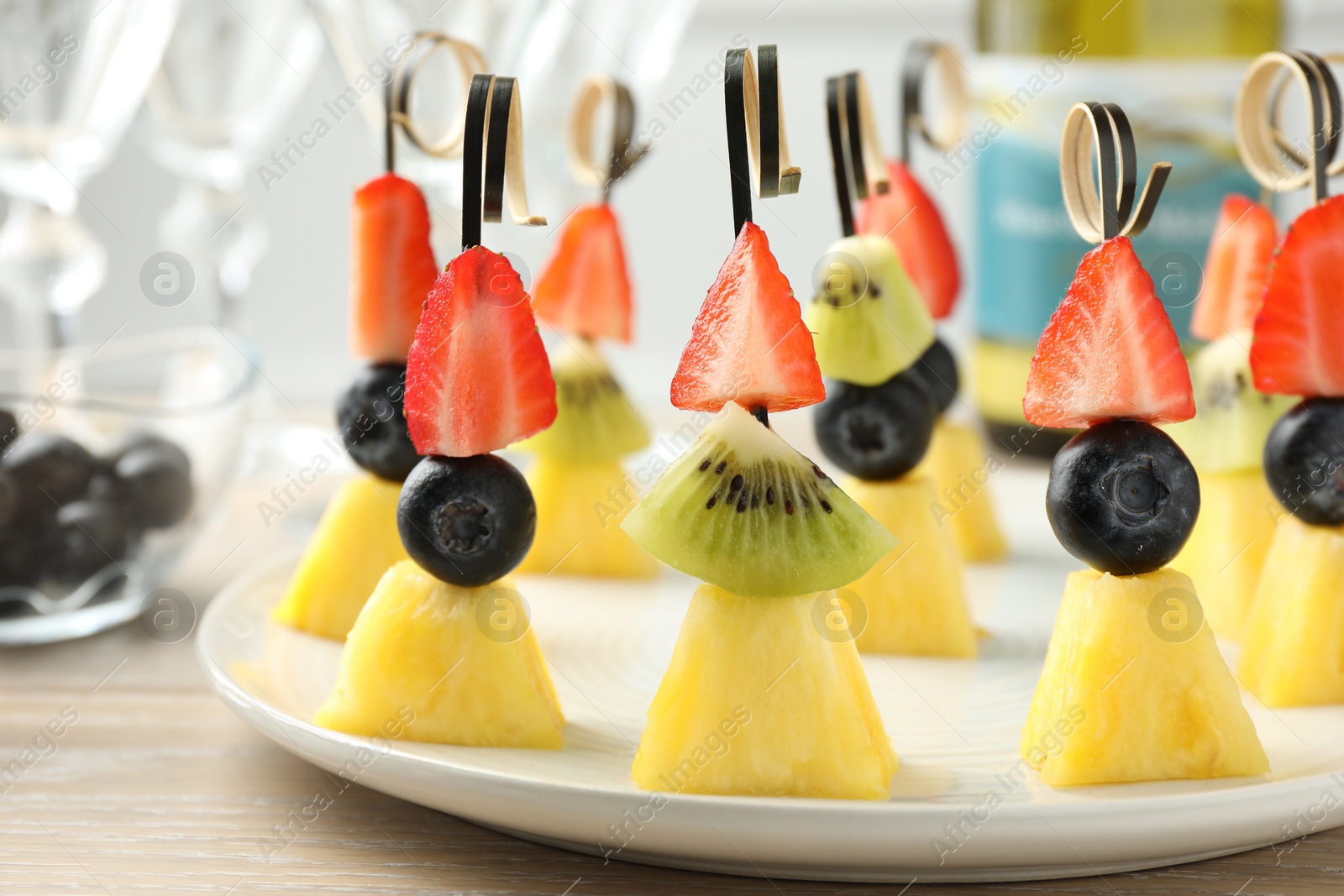 Photo of Tasty canapes with pineapple, kiwi and berries on light wooden table, closeup