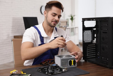 Photo of Male technician repairing power supply unit at table indoors