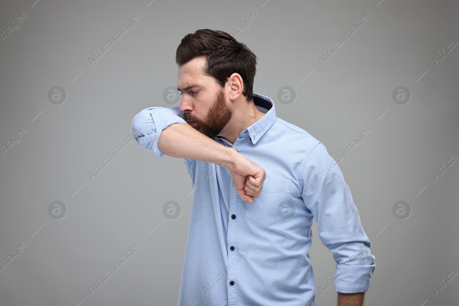 Photo of Sick man coughing into his elbow on light grey background. Cold symptoms