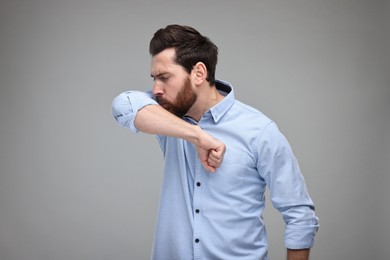 Photo of Sick man coughing into his elbow on light grey background. Cold symptoms