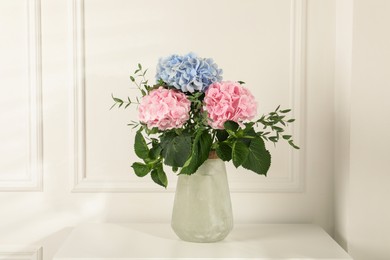 Photo of Beautiful hortensia flowers in vase on table near white wall