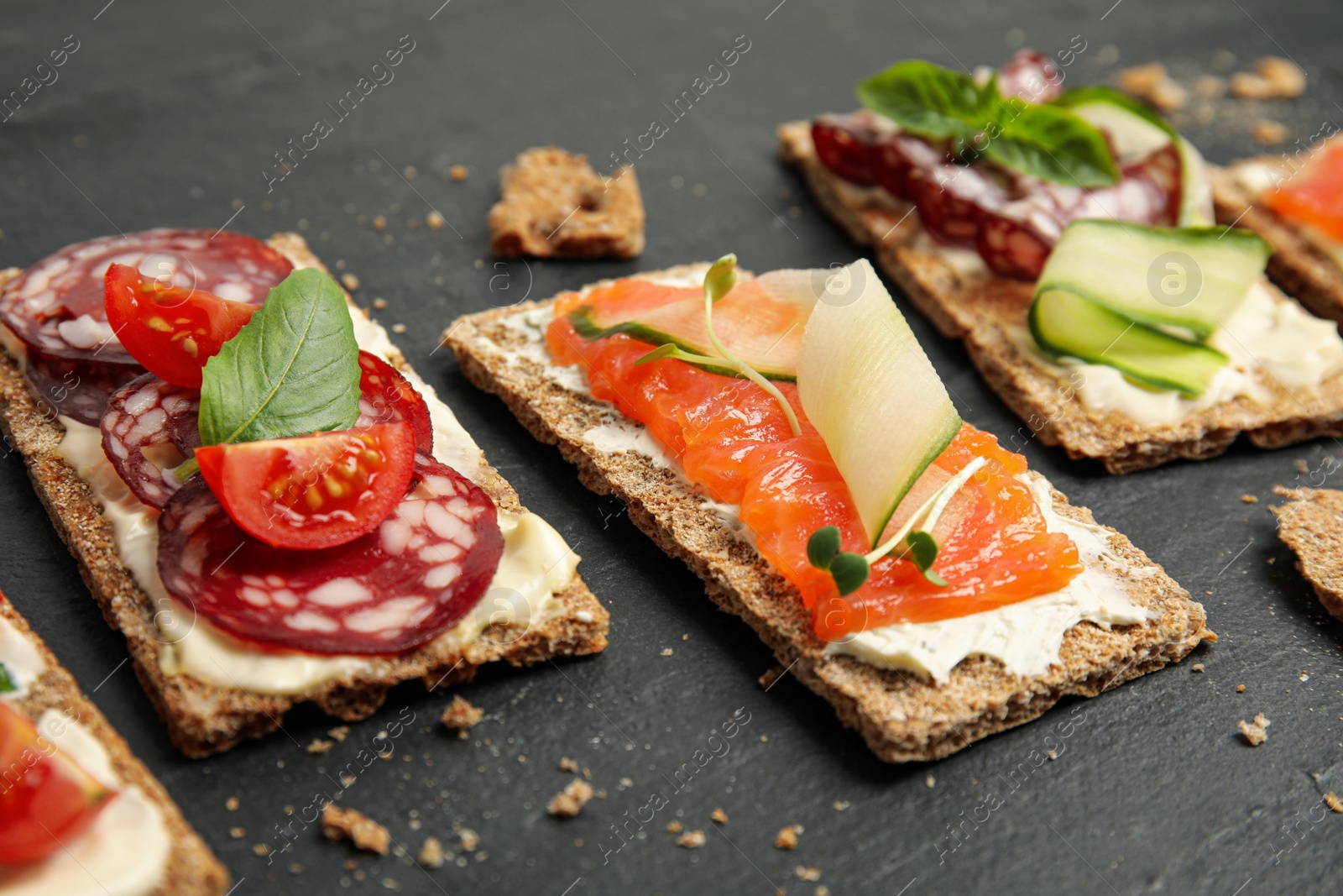 Photo of Fresh rye crispbreads with different toppings on black table, closeup