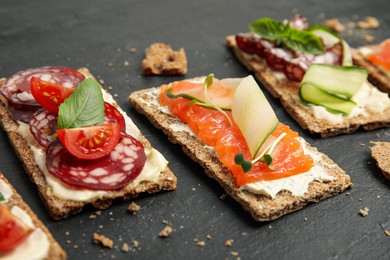 Photo of Fresh rye crispbreads with different toppings on black table, closeup