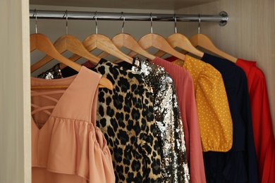 Photo of Different stylish party dresses on hangers in wardrobe, closeup