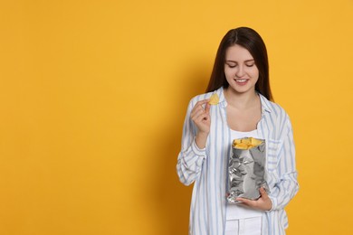 Photo of Pretty young woman with bag of tasty potato chips on yellow background. Space for text